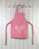 Pink child apron with gingham heart shaped pocket. From TurQuaz.