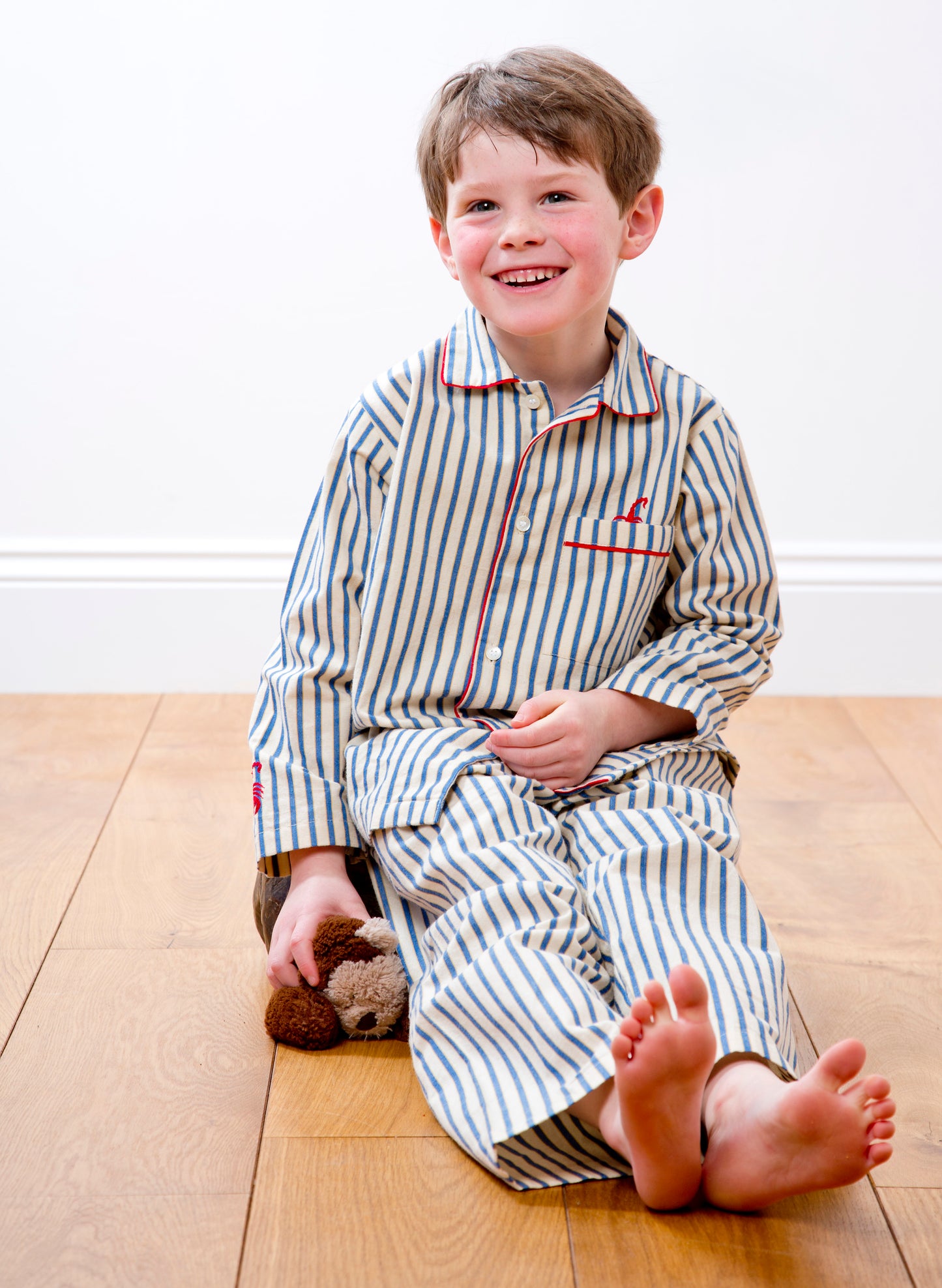 A handsome young fellow wearing traditional striped cotton pyjamas on a wooden floor with a somewhat squished stuffed toy