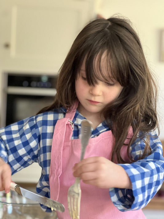 "Close-up of a child in a pink TurQuaz apron mixing banana bread batter with a fork