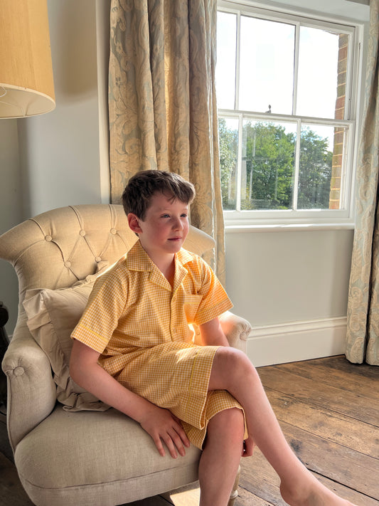 A boy sat in an armchair wearing classic yellow gingham cotton pyjamas by TurQuaz.