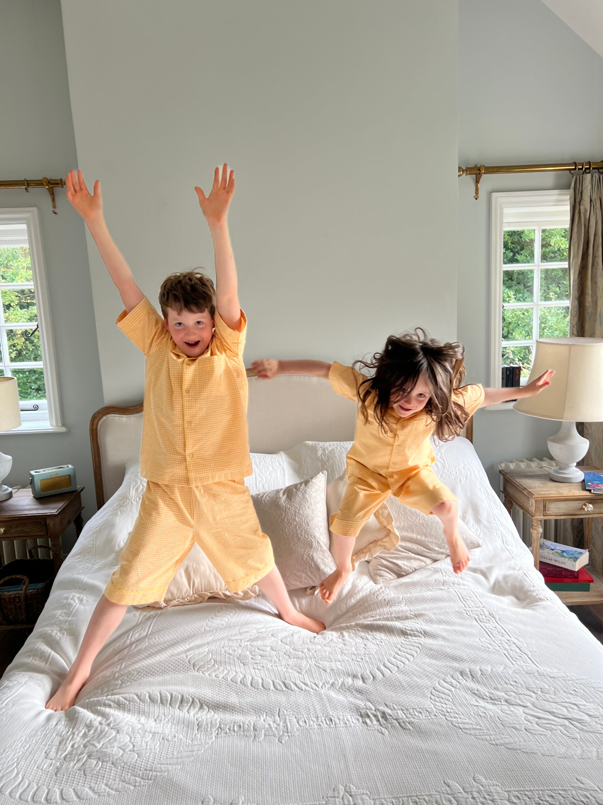 Children jumping on a bed wearing classic cotton lemon candy yellow gingham pyjamas by TurQuaz.