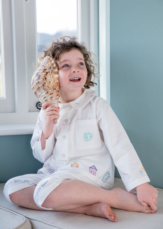 Classic pure cotton pyjamas inspired by the sea and worn by a little girl listening to the waves from a shell